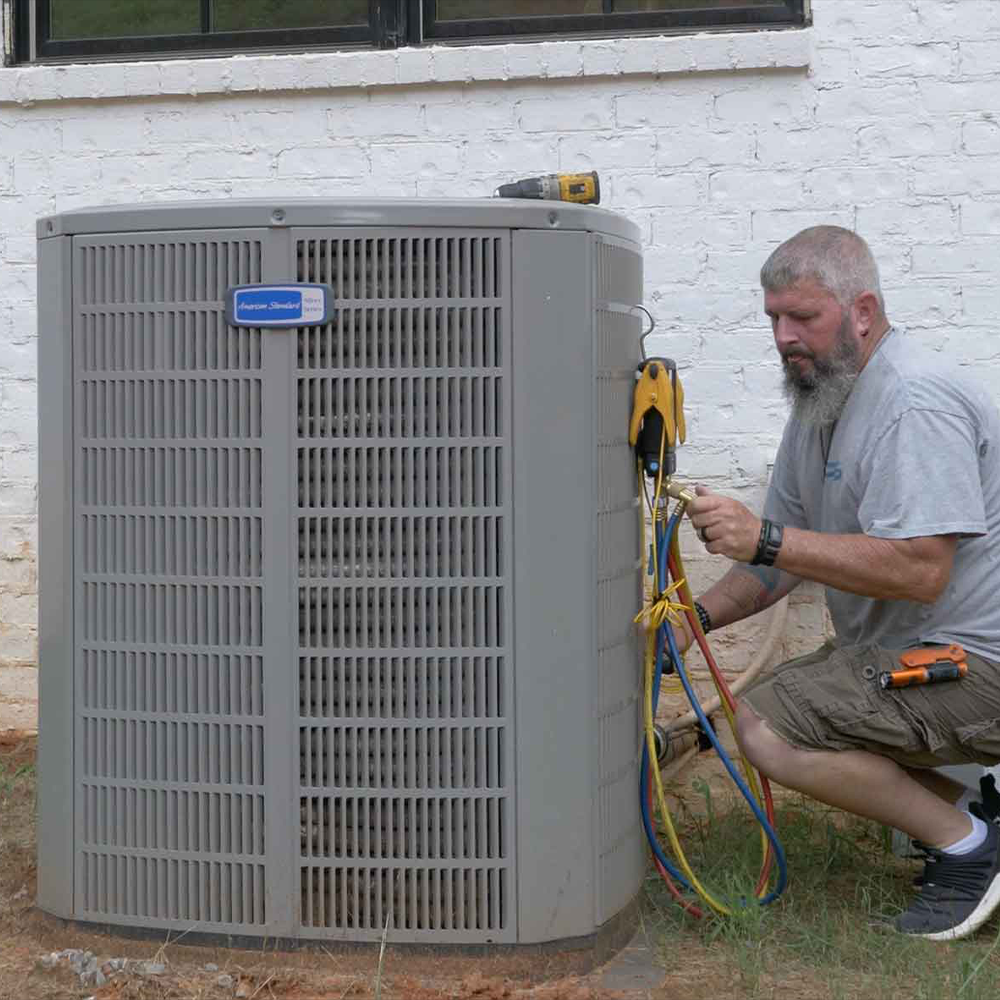 Technician servicing outdoor HVAC unit with gauges for maintenance.