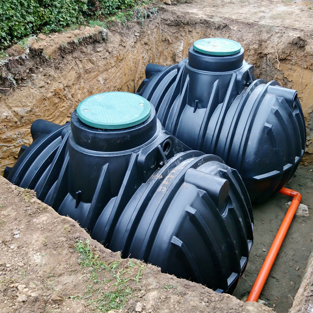 Two black septic tanks with pipes installed in soil.