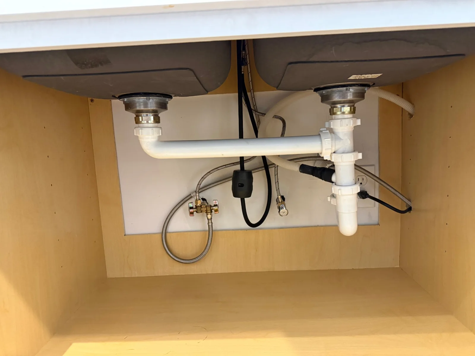 Resealed basket strainers and reassembled PVC drain assembly under a kitchen sink.