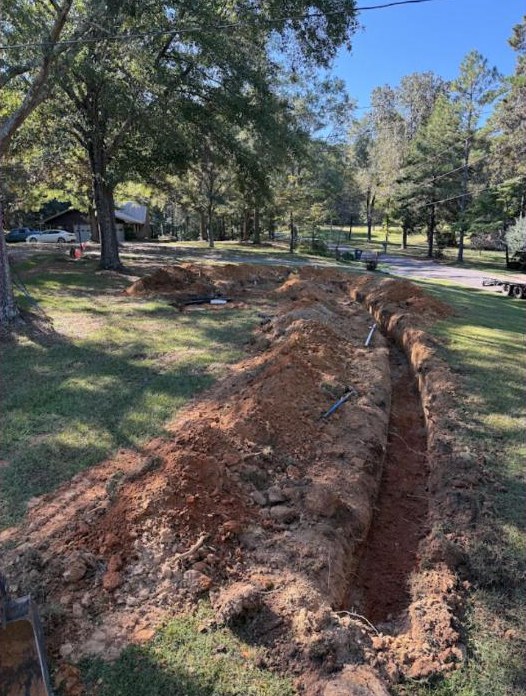 A long trench dug through a grassy residential yard.