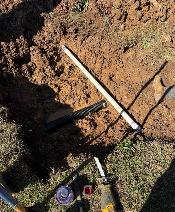 Excavated hole with PVC pipe, primer and saw ready for an underground line repair.